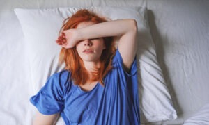 Young woman lying in bed with migraine and sensitivity to light covering her eyes