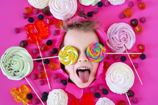 Male child with lollipops and other sugary sweets against a pink background