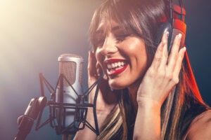 Portrait of a happy young woman singer with headphones in front of studio microphone.