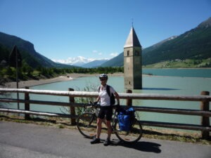 Picture of smiling female cyclist on the Via Claudia Augusta bikepath at Lake Reschen on a sunny day