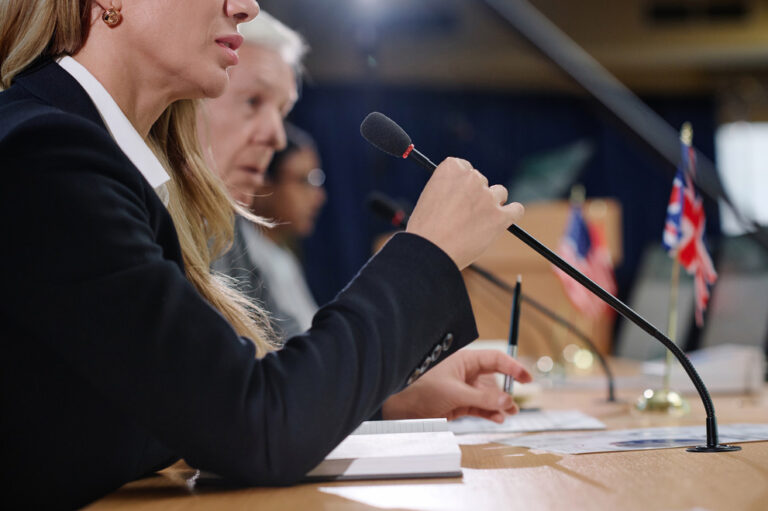 Woman in a suit speaking into microphone at a business meeting